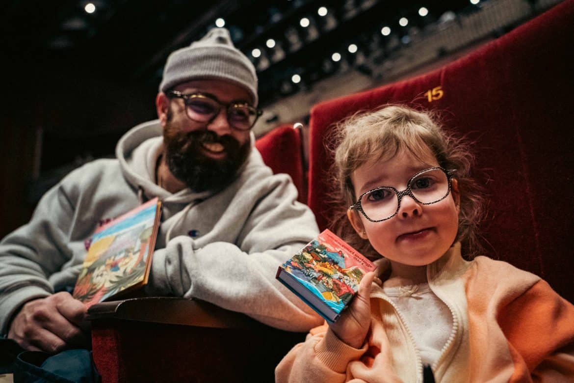 Un enfant et un adulte en gros plan qui montrent le dépliant jeunes publics et un bloc note 2024