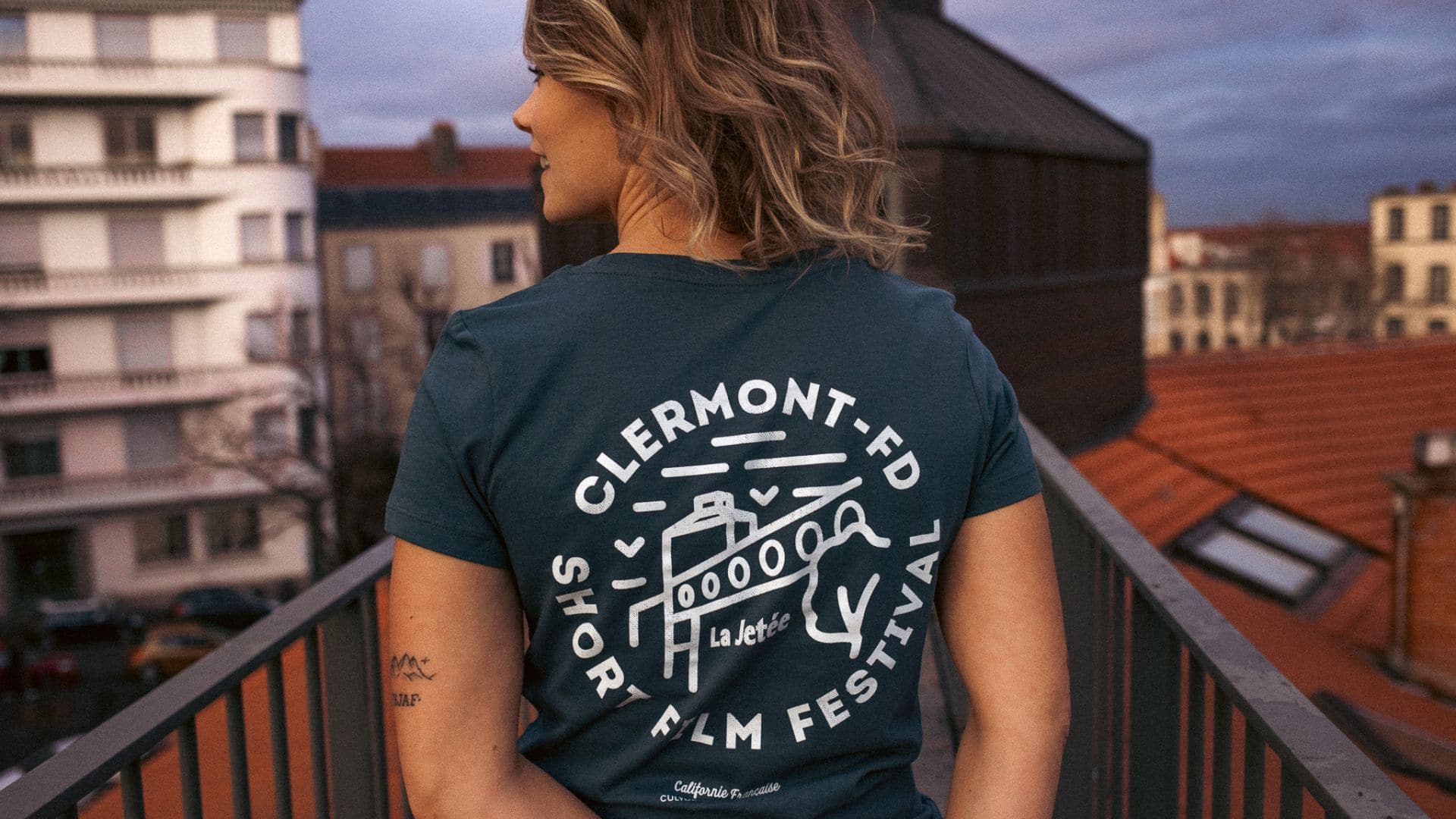 Une jeune femme de dos porte un t-short "La Jetée" en collaboration avec la marque Californie française